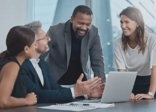 Four employees collaborating and standing around a desk and laptop.