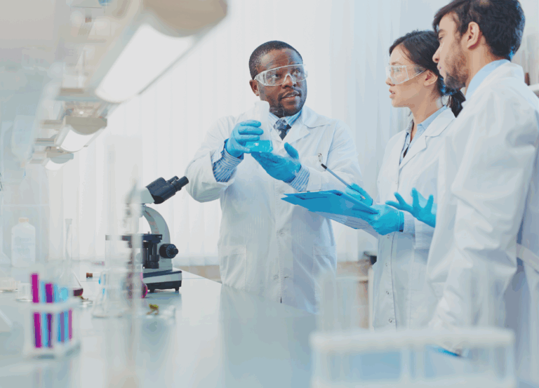 Three lab techs in coats and gloves in front of a microscope for clinical trials.