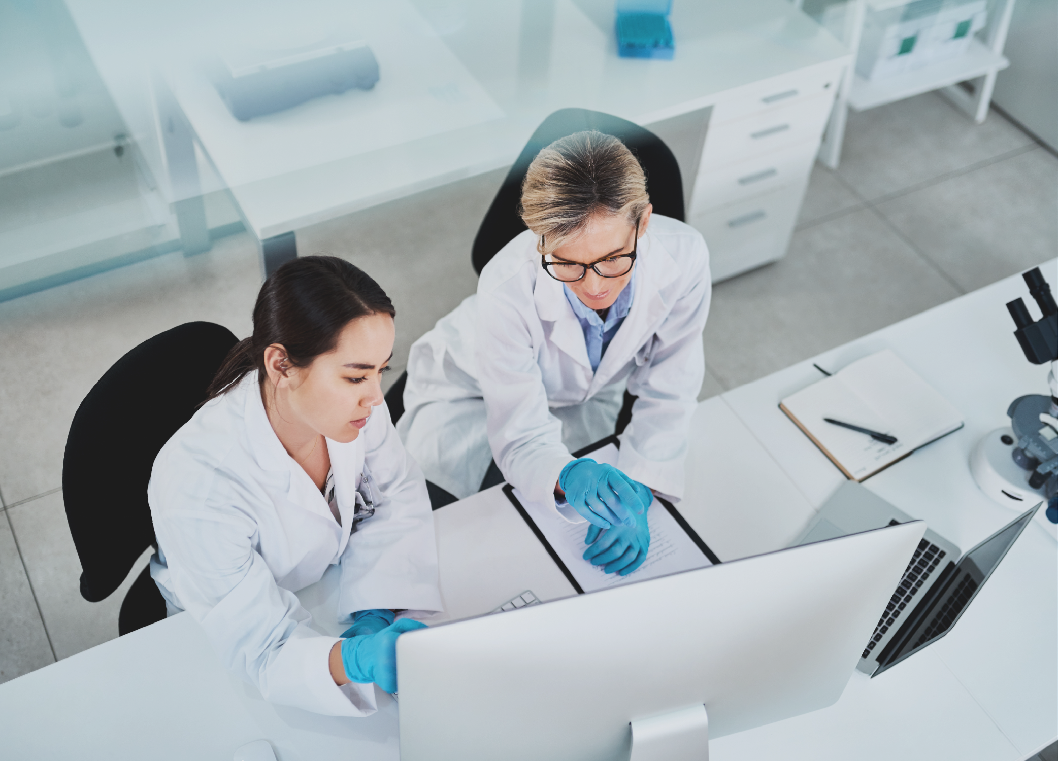 Two women medical lab techs looking at a computer monitor as part of clinical trial management.