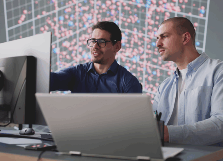 Two men, one on a laptop, one on a desktop, looking at computer screens.