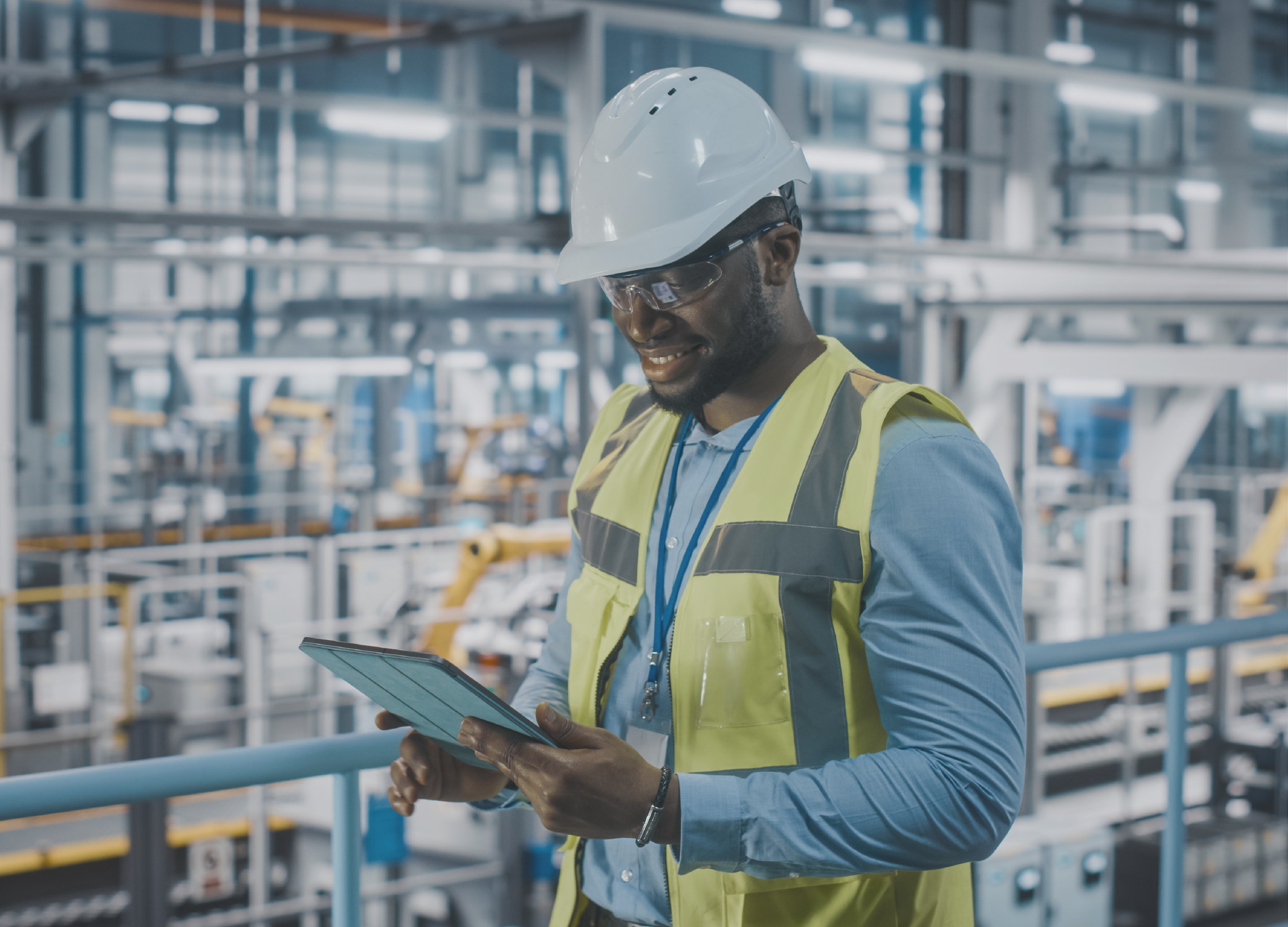 Man in hardhat and wearing a yellow vest taking inventory in a warehouse.