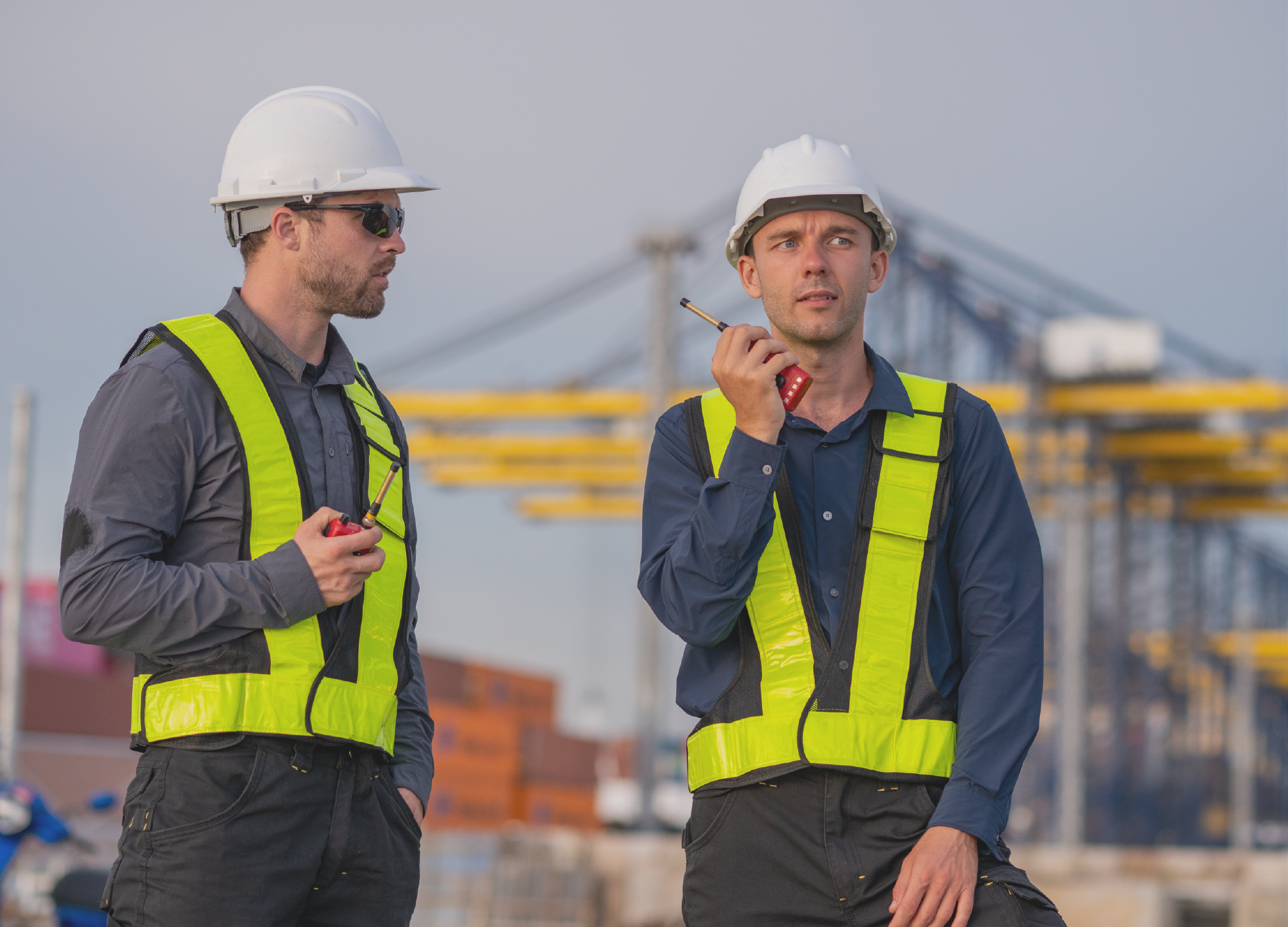 Two employees with walkie talkies with yellow vests and hardhats on managing supply chains.