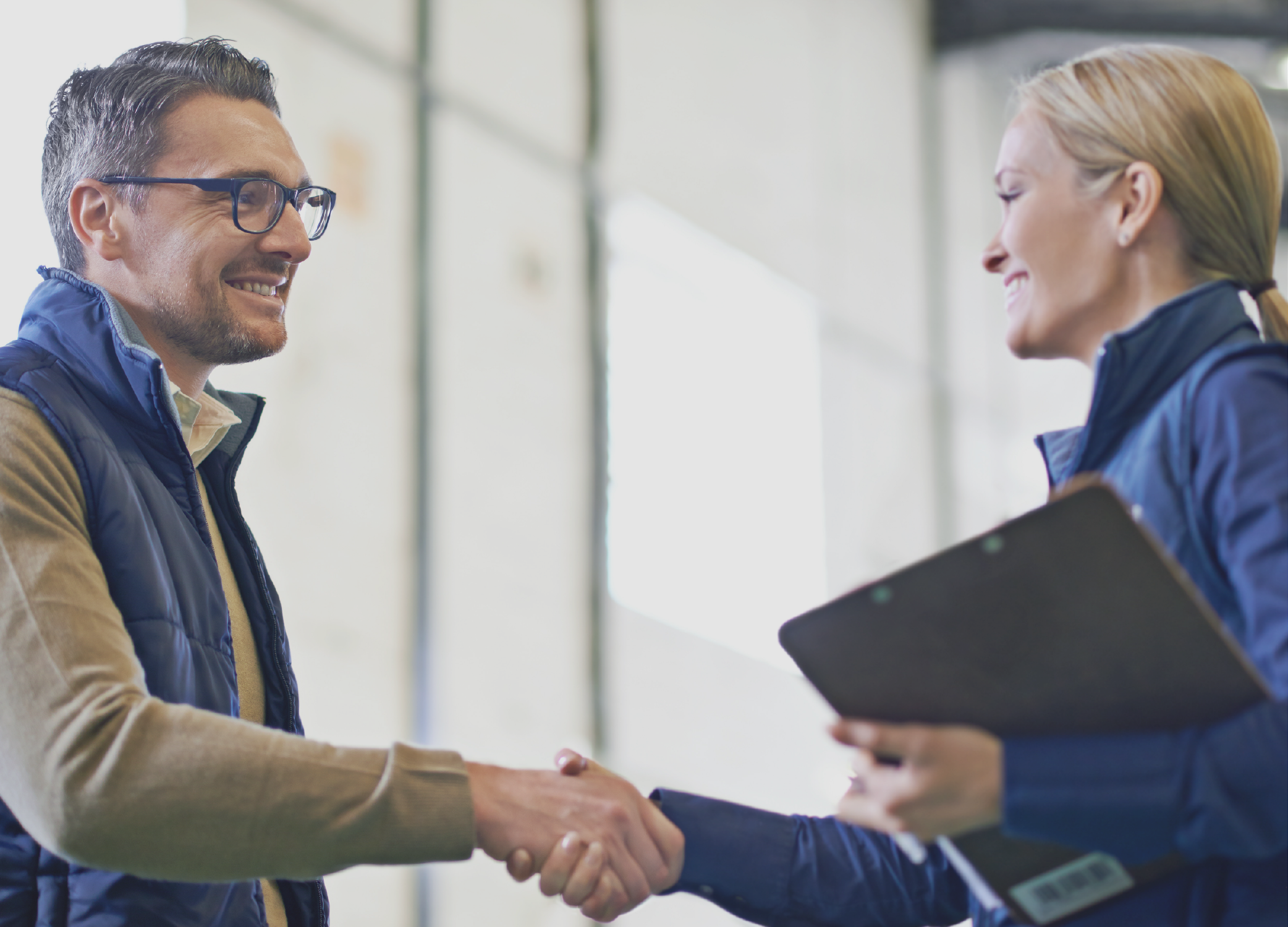 Man and a woman shaking hands, the woman holding a clipboard.
