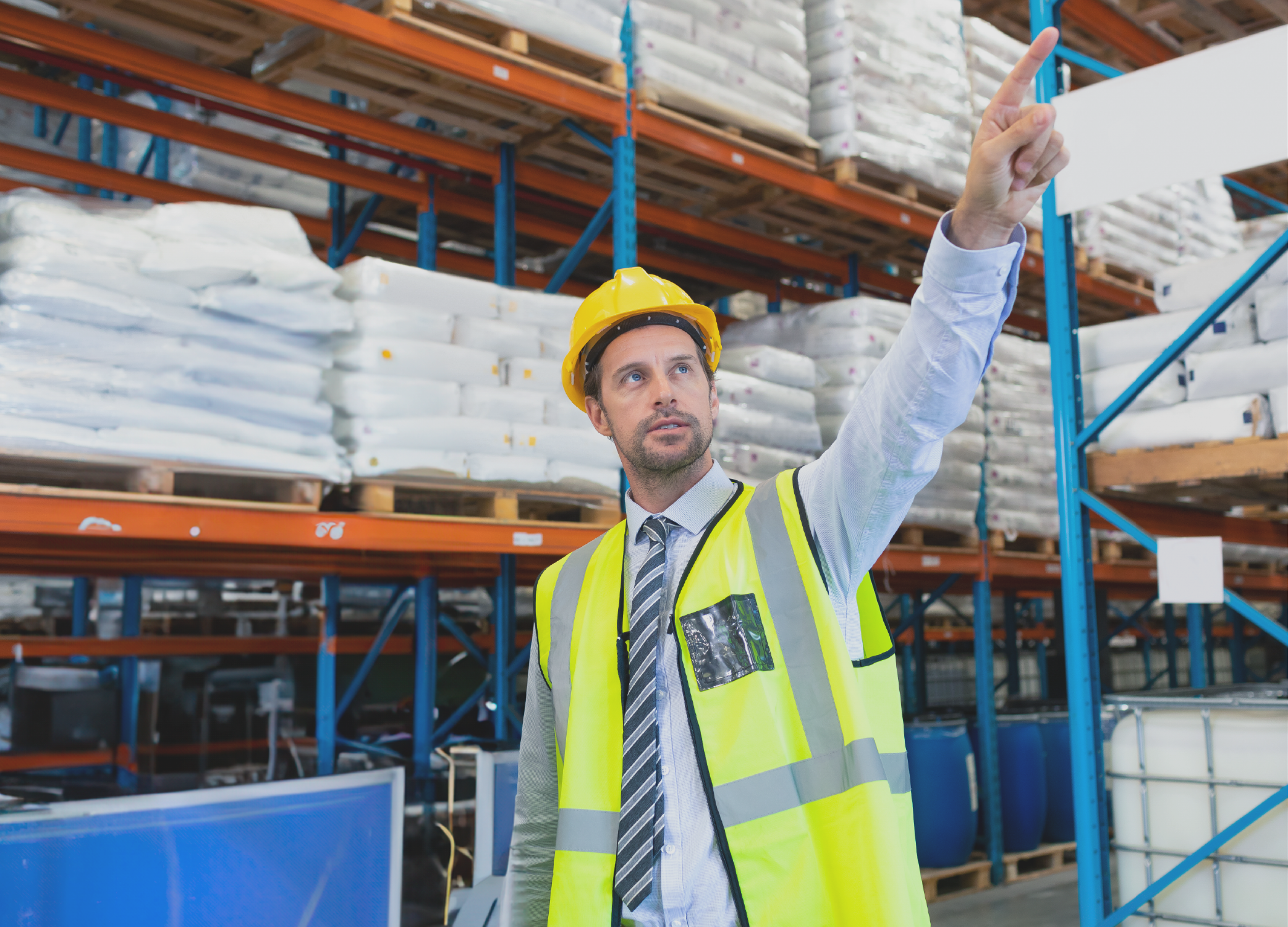Man in a hard hat and yellow vest pointing while working in a warehouse.