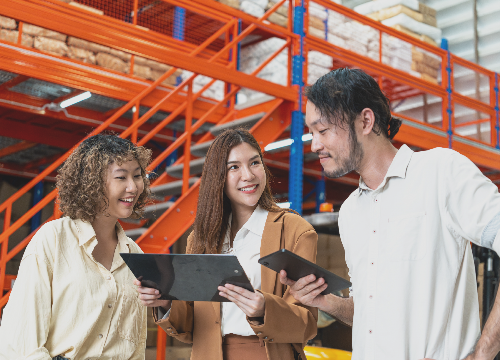 Three employees, two women and looking at tablets while in a warehouse.