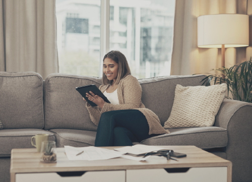 Woman working from home using a tablet while sitting on a sofa in an apartment.