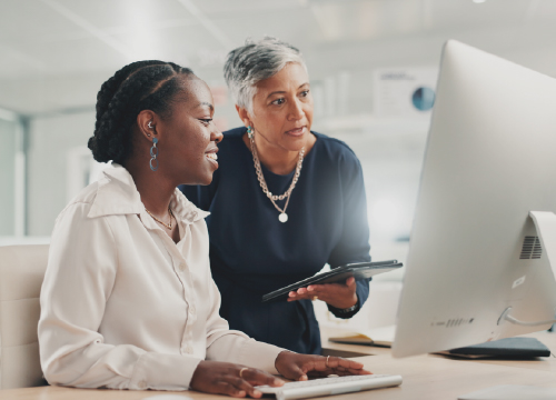 Two women collaborating and looking at Exostar careers on the website.