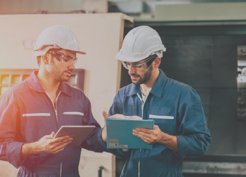 Two employees collaborating in coveralls and wearing hardhats.