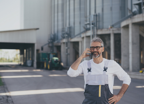 A man in overalls smiling and talking on a cell phone outside a building.