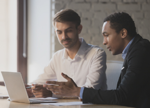 Two employees securely collaborating and looking at a laptop.