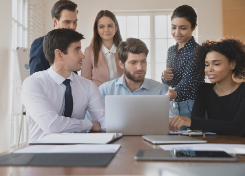 Six employees all around a conference table and looking at a laptop screen.