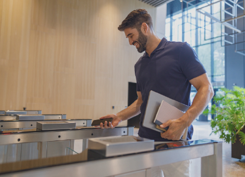 Male employee holding a laptop and notebook while looking down at his phone.