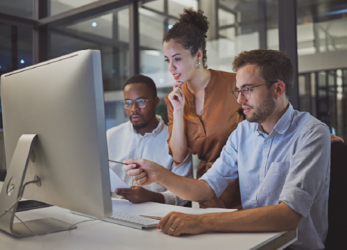 Three employees collaborating and looking at a large computer monitor.