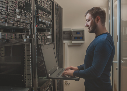 A man typing on a laptop in a server room in secure isolation.