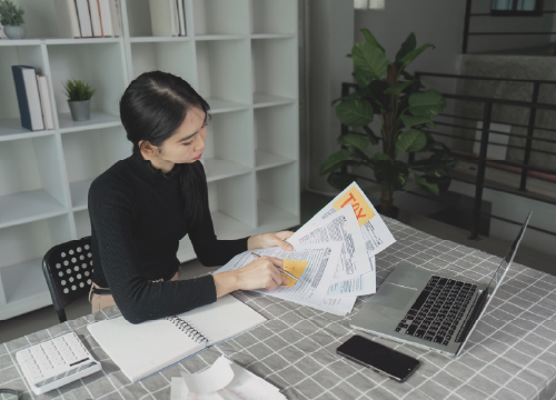 A female employee working securely from home with a laptop and papers on the table.