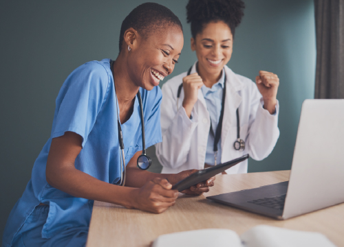 Two healthcare workers looking at a laptop screen and celebrating results.