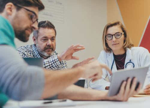 Three healthcare employees looking at a tablet and collaborating.