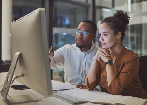 Man and woman collaborating in front of a computer monitor.