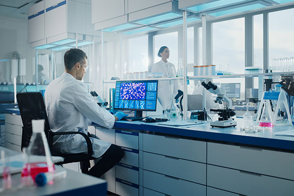 A medical lab technician staring at data on a computer screen.