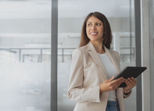 Business woman in front of a window holding a tablet.