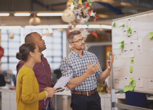 Certification assistant header image of three people collaborating in front of a whiteboard.