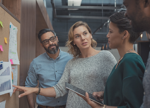 Three workers, two women and one man, looking at information on a pinup board.