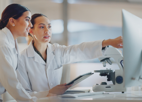 Two women in lab coats looking at a computer screen.