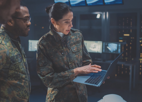 A man and a woman in military garb looking at a laptop for secure defense needs.