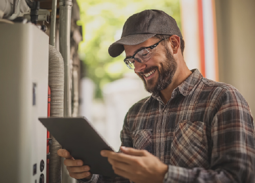 A man in a hat and flannel shirt looking at a tablet while working.