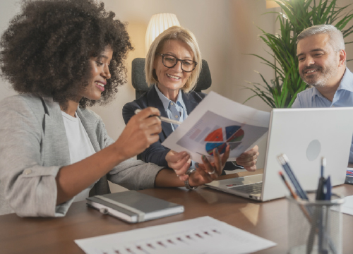 Two women and a man looking at charts and sitting around a conference table.