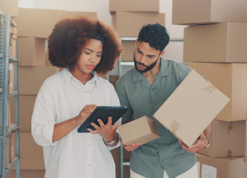 Two employees in a warehouse managing supplies and looking at a tablet.