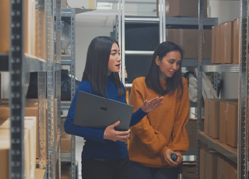 Two women looking at products on a shelf in a warehouse.